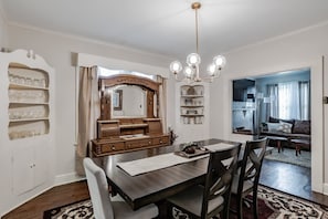 A dining area with a wooden table and chairs, a chandelier, and a mirror above the table.