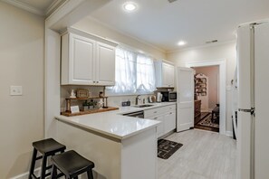 A kitchen with white cabinets, a central island with stools, a microwave, and a refrigerator. - Midtown Cottage, Great Location! Haute on Hannon (Mobile)