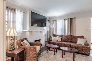 A living room with a fireplace, two sofas, a coffee table, and a television mounted above the fireplace. - Midtown Cottage, Great Location! Haute on Hannon (Mobile)