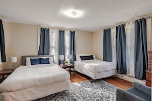 A hotel room with two beds, a nightstand with lamps, a small table with a plant, and a patterned rug.