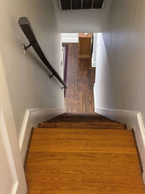 A wooden staircase with a handrail, leading to a room with a wooden floor and white walls.