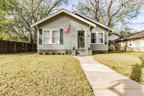 Uma casa térrea com varanda frontal, um pequeno jardim e uma bandeira americana.
