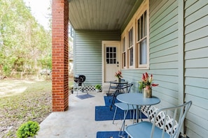 A covered porch with a grill, outdoor table, and chairs, surrounded by a fenced yard.