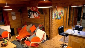 Ein gemütliches Blockhaus-Interieur mit Essbereich, einer Sofagarnitur mit orangefarbenen Kissen und Kunstwerken an den Wänden.