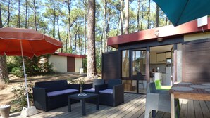 Una terraza exterior con una mesa de madera, dos sofás y un paraguas rojo.