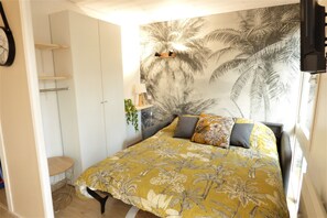 Un dormitorio con una cama, un televisor de pared, un estante y una mesita.