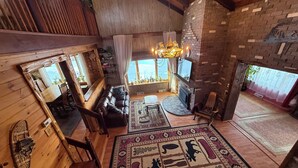 A cozy cabin interior with a fireplace, wooden furniture, and a large rug with animal prints. - Spacious Adirondack House in Otter Lake (Forestport)