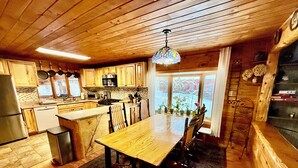 A kitchen with wooden cabinets, a dining table, and a hanging light fixture. - Spacious Adirondack House in Otter Lake (Forestport)