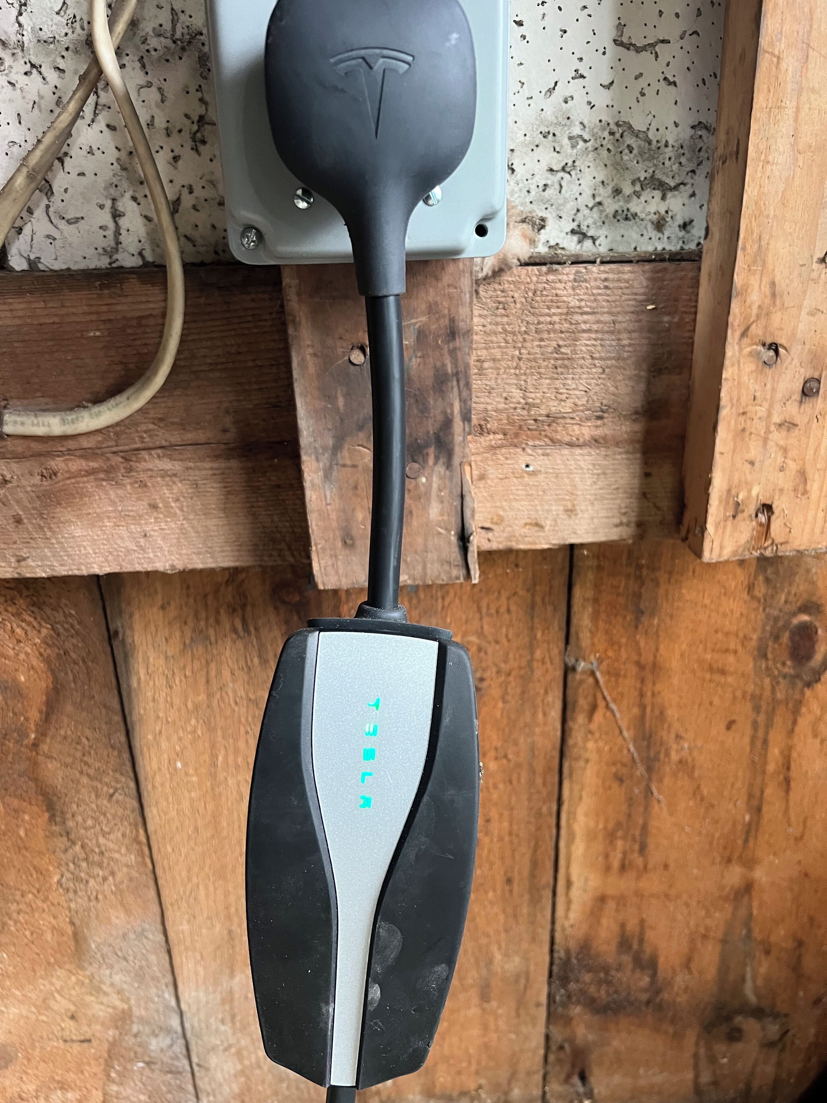 A black and silver electric vehicle charging station mounted on a wooden wall.