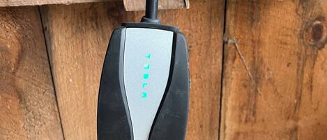 A black and silver electric vehicle charging station mounted on a wooden wall.