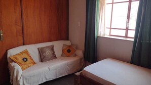 Una habitación con un armario de madera, un sofá blanco con cojines y una cama.