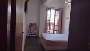 Un dormitorio con cama, una silla, una ventana con cortinas y una puerta.