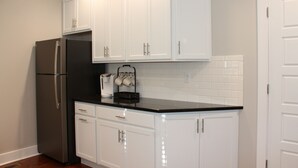 Cocina con armarios blancos, encimera negra y refrigerador de acero inoxidable.