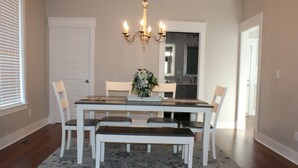 Un comedor con una mesa rectangular, sillas blancas, un banco y una araña.