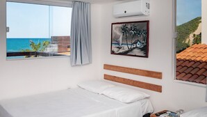 A hotel room with a bed, a window with a view of the sea, a painting on the wall, and an air conditioning unit. - Hotel Pousada Encanto da Praia  (Natal)