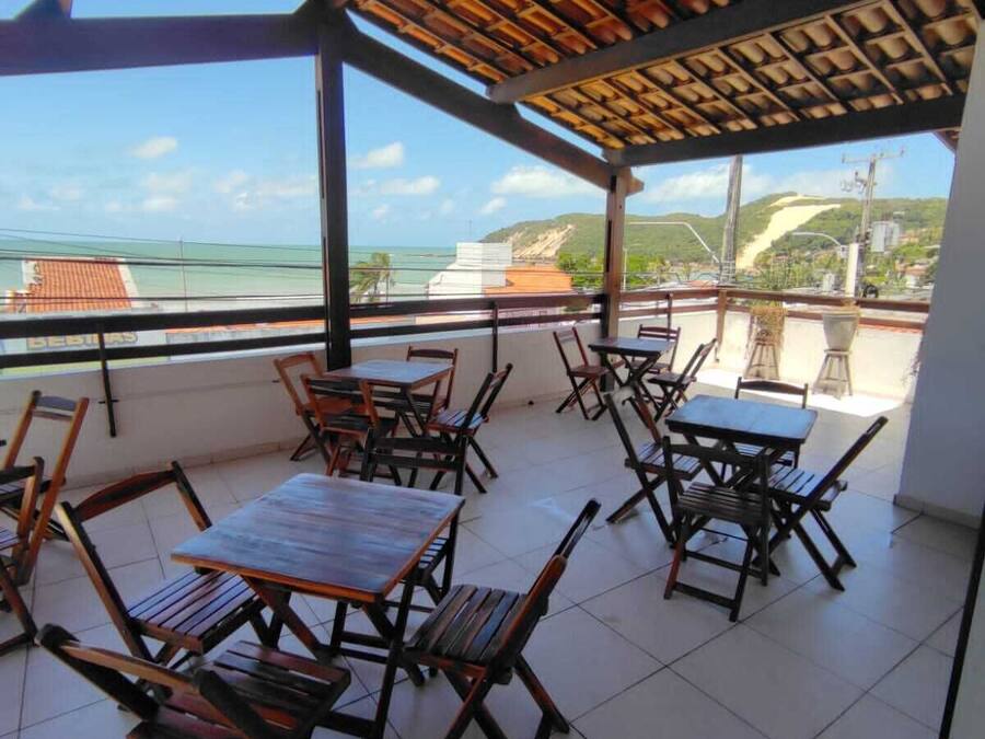 A covered outdoor seating area with tables and chairs, overlooking a scenic view of the ocean and a distant hill.