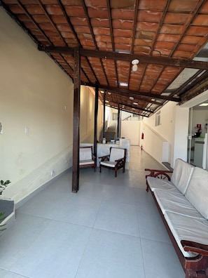 Um corredor com piso de azulejos, bancos de madeira, um balcão de recepção e uma escadaria para um andar superior.
