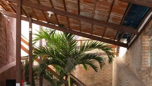 A covered outdoor area with a wooden bar, stools, a staircase, and a large palm tree. - Hotel Pousada Encanto da Praia  (Natal)