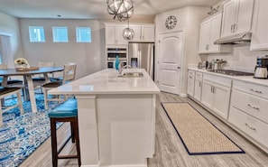 Una cocina con una isla grande, armarios blancos, electrodomésticos de acero inoxidable y un tapete azul estampada.
