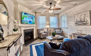 A living room with a fireplace, two armchairs, a sofa, a coffee table, a TV, and a ceiling fan. - Ocean View * 5BR Luxury Single Family House! (Ocean View)