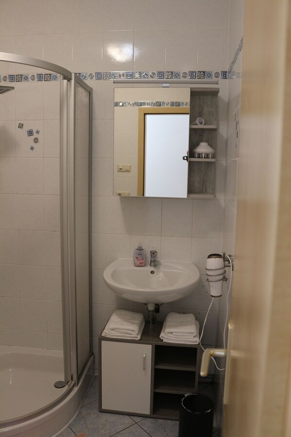 A bathroom with a shower, sink, and cabinet.
