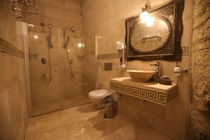 Casa de banho com chuveiro envidraçado, sanita, lavatório com cuba decorativa e espelho com moldura ornamentada.