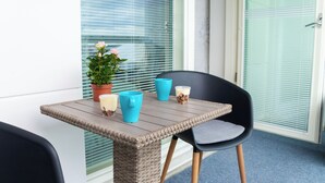 Ein Balkon mit einem Korbstuhl-Tisch, zwei Stühlen, einem Blumentopf und einer Tür mit Milchglasfenster.