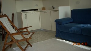 A compact kitchen with white cabinets, a blue sofa, and a wooden chair. - Two-room apartment in the countryside a stone's throw from the sea (Calice Ligure)