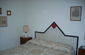 Cozy retreat with a geometric headboard and patterned bedspread, featuring a nightstand with a lamp and framed picture.
