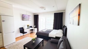 Une chambre d’hôtel moderne équipée d’un lit, d’un bureau, d’une chaise, d’une petite table avec une plante et d’un téléviseur fixé au mur.