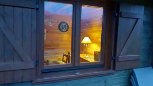 Eine Holzhütte mit einem großen Fenster, darin eine Uhr und ein Tisch mit einer Lampe.