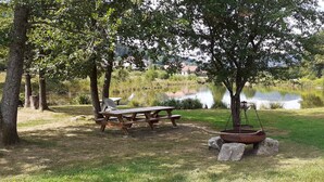 Ein Picknickplatz mit Tisch und Bänken, umgeben von Bäumen und einem Teich.