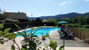 Ein Schwimmbecken mit Bergblick, umgeben von einem Zaun und Liegestühlen.