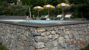 Area piscina con pareti in pietra, lettini e ombrelloni.