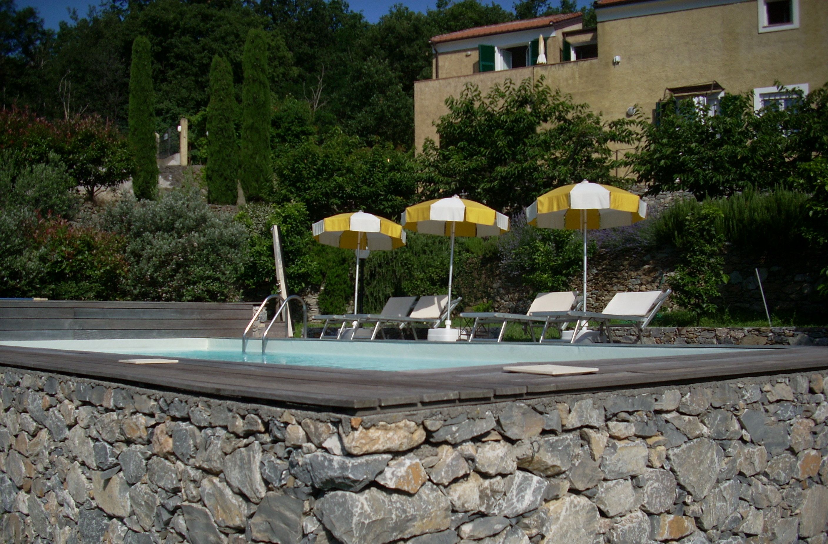Area piscina con pareti in pietra, lettini e ombrelloni.