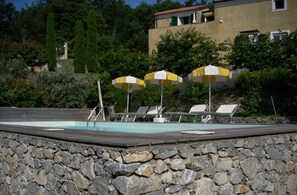 A pool area with stone walls, lounge chairs, and umbrellas.