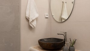 A bathroom with a round mirror, a vessel sink, and a towel rack. - Aqua Naxos Apartments and Suites (Naxos)