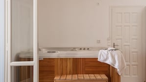 A room with a wooden bench, a white bathtub, and a wooden ceiling light fixture. - Aqua Naxos Apartments and Suites (Naxos)