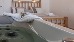 A modern bathroom with a large bathtub, wooden headboard, and wall-mounted lights. - Aqua Naxos Apartments and Suites (Naxos)