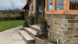 A stone house with a wooden porch, large windows, and a stone pathway leading to the entrance. - Meagill Farmhouse, hot Tub, bbq hut (Otley)