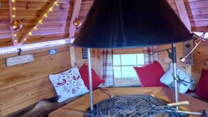 A cozy cabin interior with a wooden ceiling, string lights, a fireplace, and red and white pillows. - Meagill Farmhouse, hot Tub, bbq hut (Otley)