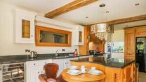 A modern kitchen with a central island, wooden cabinets, and a dining area with chairs. - Meagill Farmhouse, hot Tub, bbq hut (Otley)