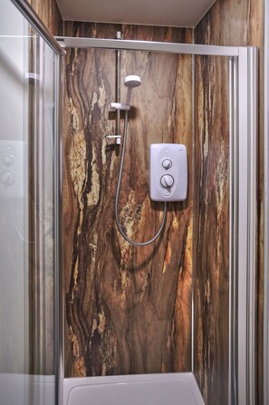 A shower with a marble wall, a handheld showerhead, and a control panel.