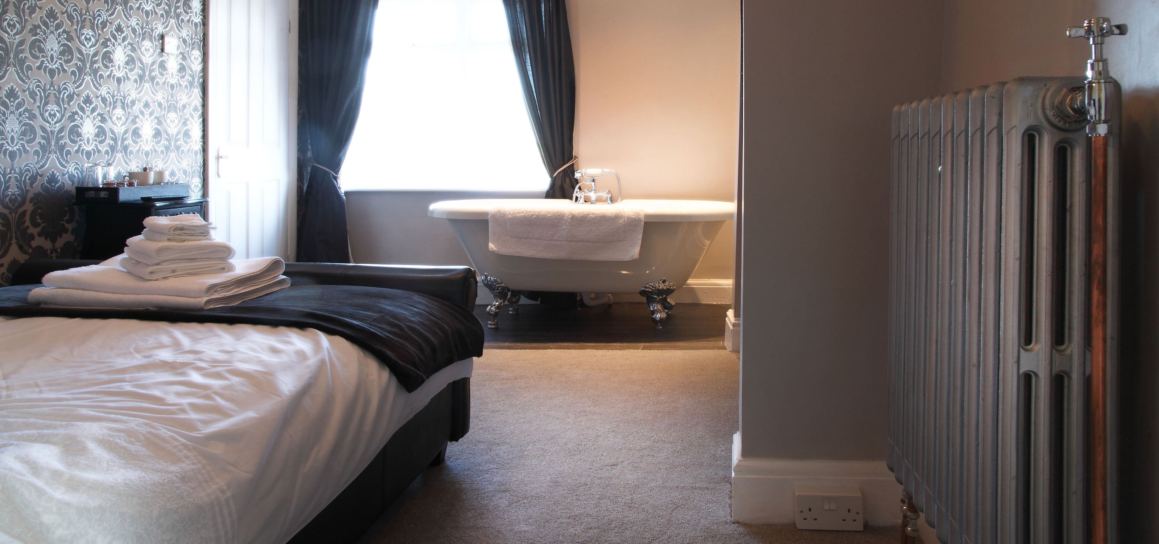 A bedroom with a bed, a radiator, a bathroom with a bathtub, and a window with curtains.