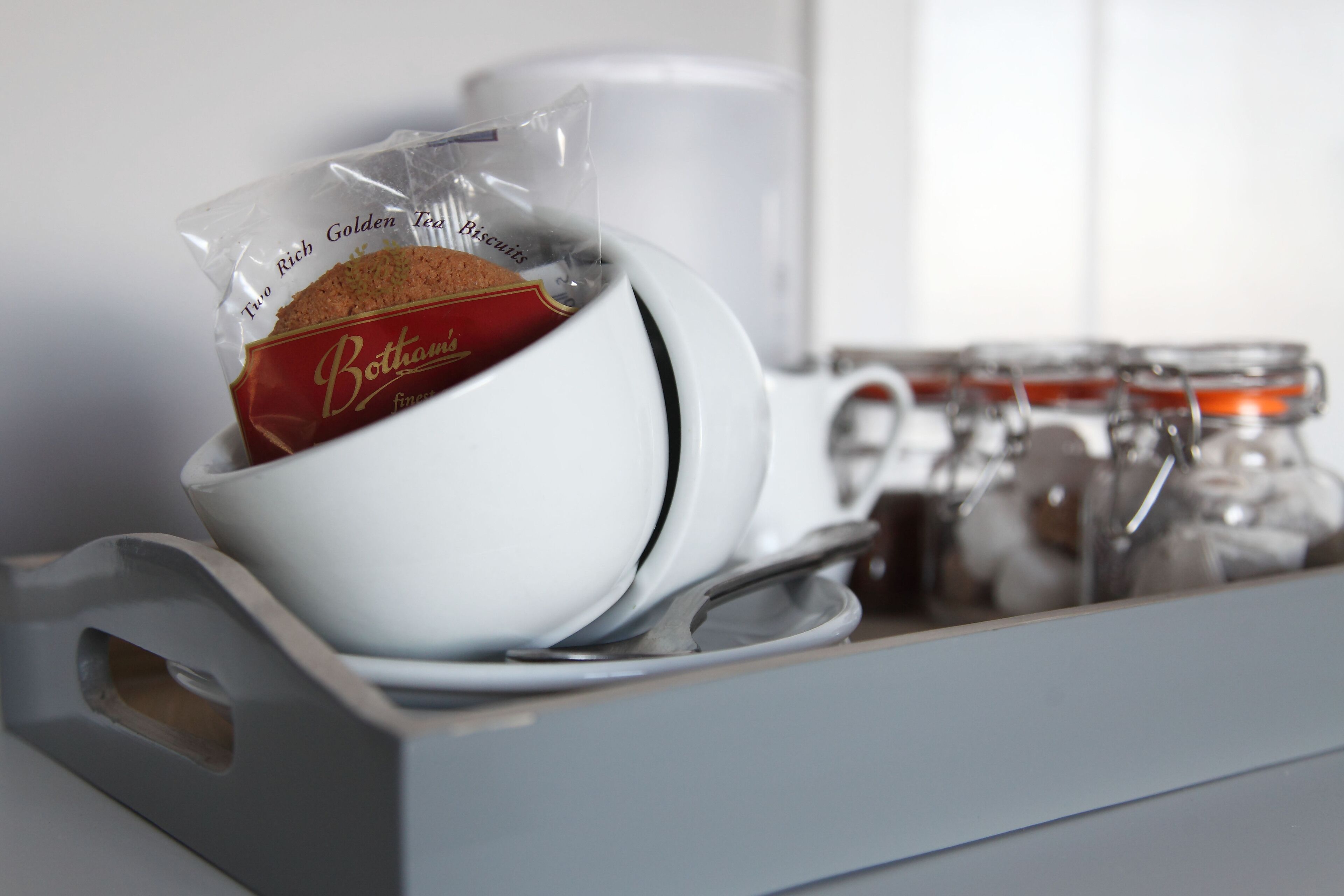 A tea set with a bag of tea and biscuits, a white cup, and a row of glass jars.