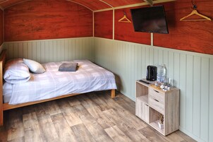 Una cama individual con un edredón a cuadros, una mesita de noche con una tetera y vasos, y un mueble de madera con una planta.