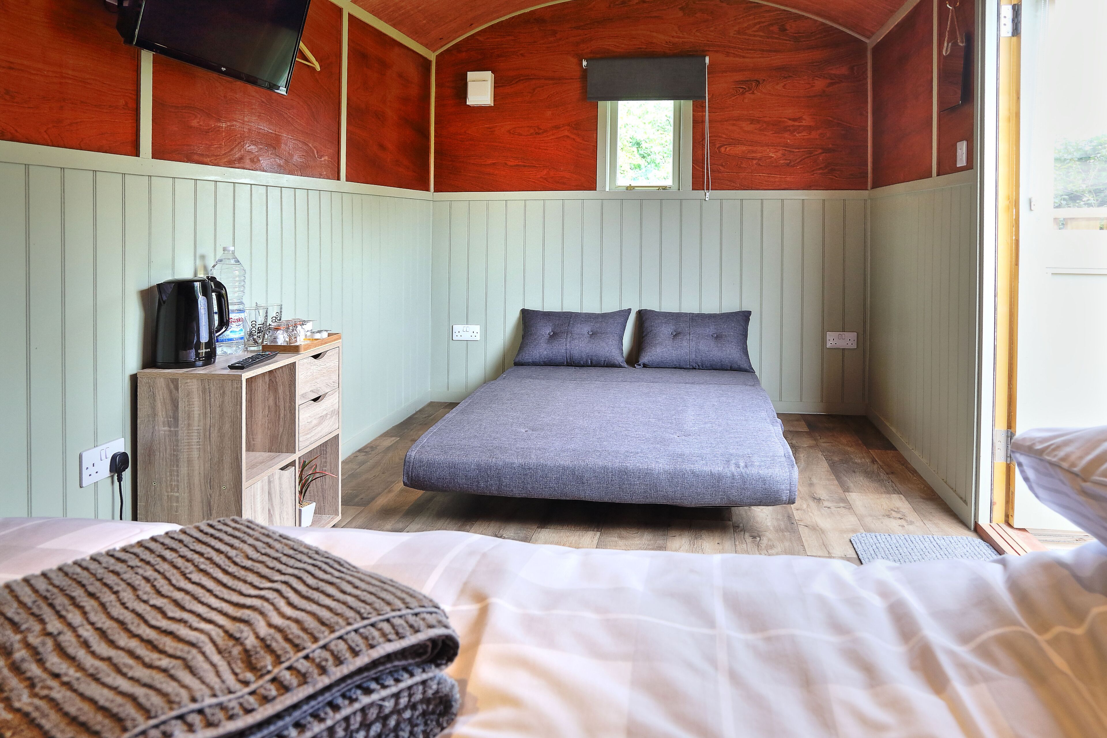 A bedroom with a bed, a wooden dresser, a television, and a window.