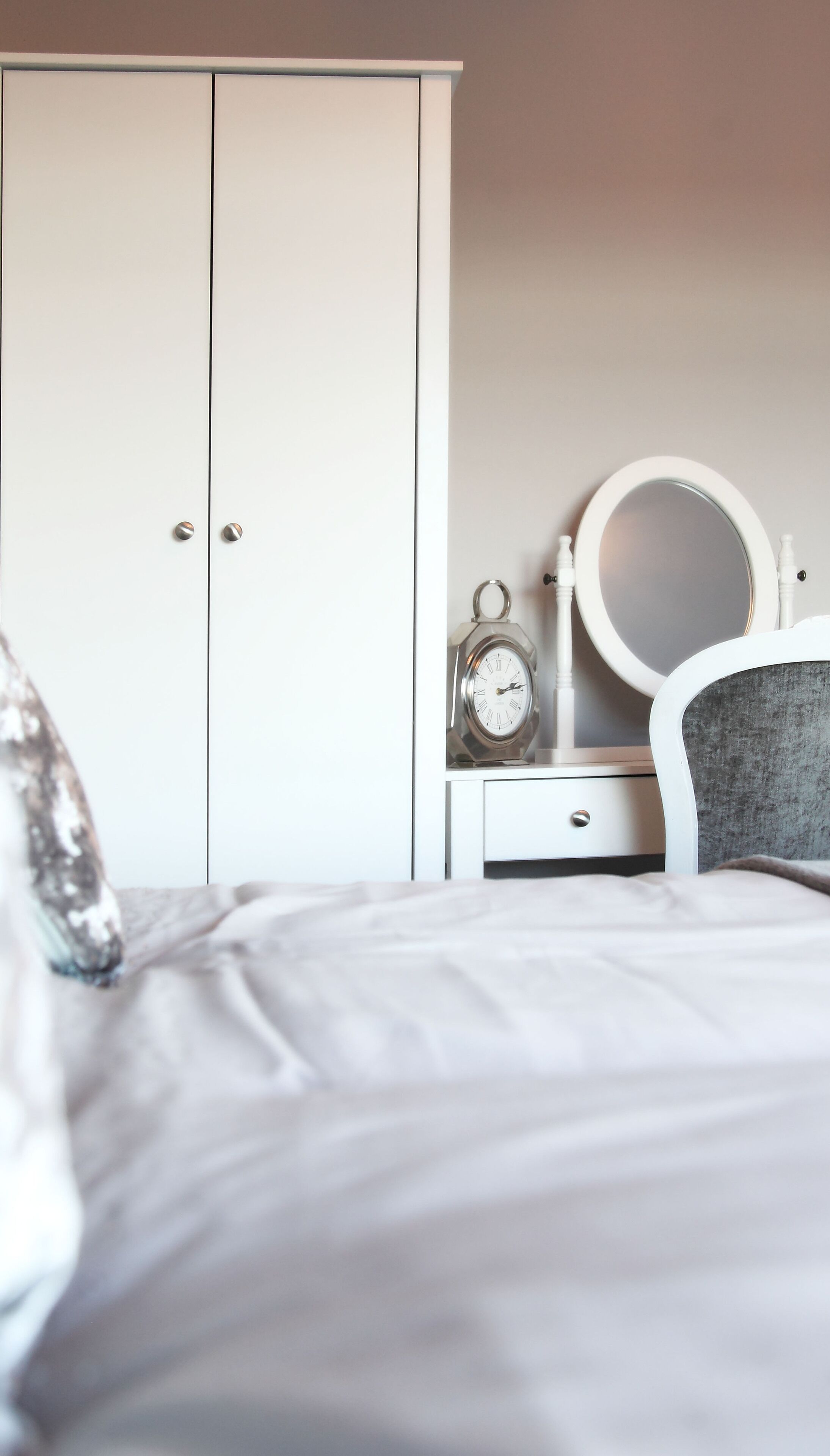 Ein Schlafzimmer mit einem Bett, einem Kleiderschrank, einem Nachttisch mit einer Uhr und einem Stuhl.