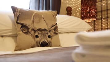 Una cama con un cojín de diseño de ciervo, una lámpara y un papel tapiz estampado al fondo.