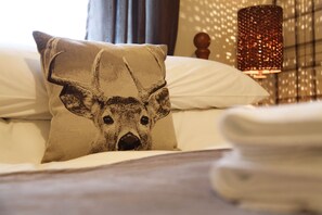 A bed with a pillow featuring a deer design, a lamp, and a patterned wall in the background.